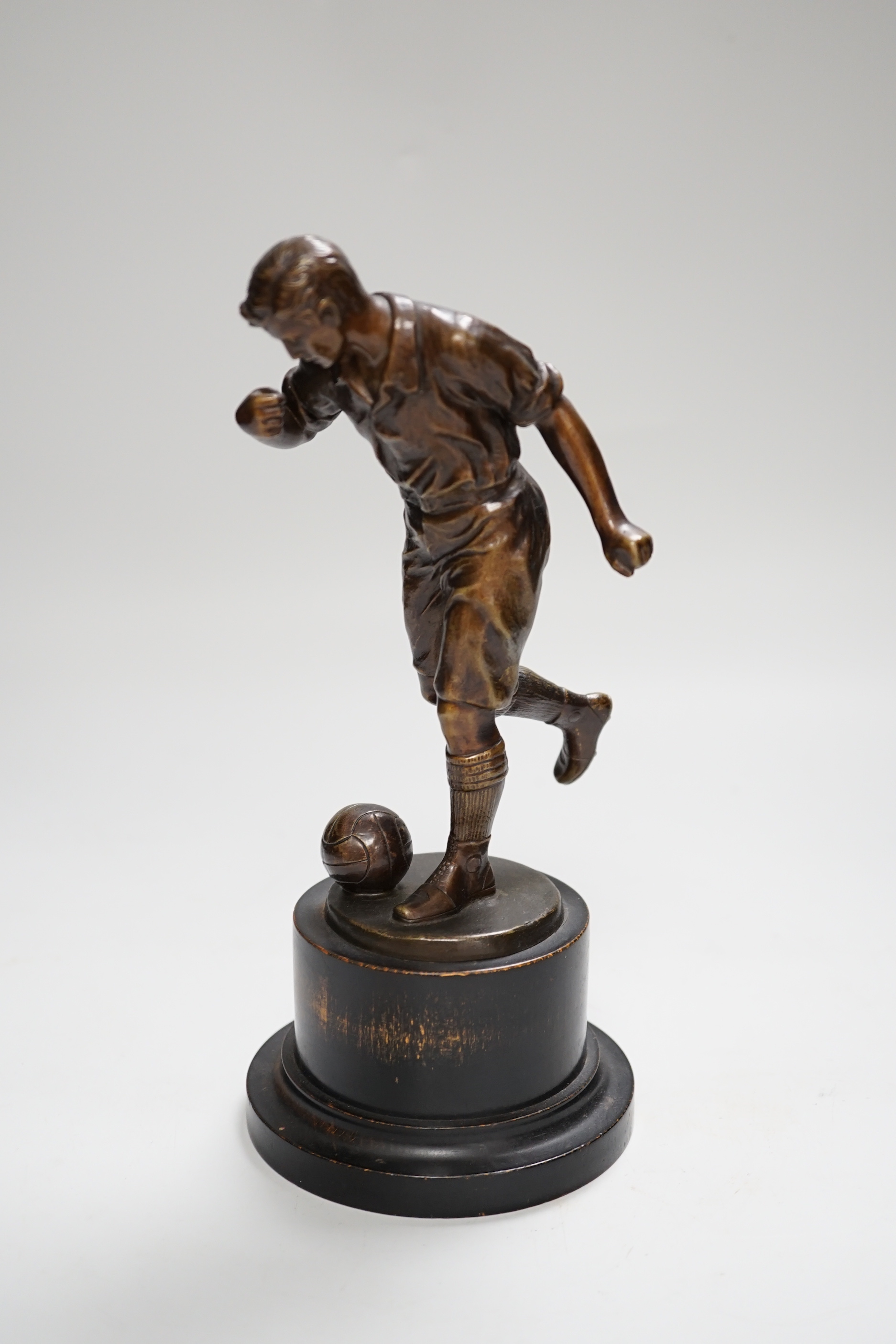 A pre-war bronze figure of a footballer, raised on a circular ebonies wood base, 23cm high